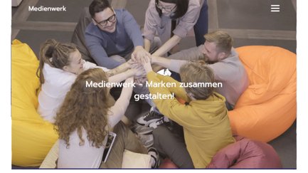 Eine Gruppe von sechs Personen sitzt auf bunten Sitzsäcken und legt ihre Hände in die Mitte, um Teamgeist zu zeigen.