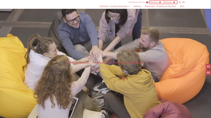 Screenshot einer Website, auf der mehrere Menschen in bunten Sesseln sitzen und sich die Hand reichen. Am oberen Rand sind zwei Topbar Actions Links  in rot eingerahmt