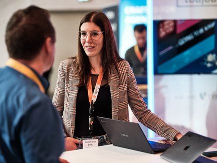 Geschäftliche Gesprächssituation zwischen einer Frau und einem Mann, im Hintergrund ein Screen