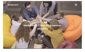 Eine Gruppe von sechs Personen sitzt auf bunten Sitzsäcken und legt ihre Hände in die Mitte, um Teamgeist zu zeigen.