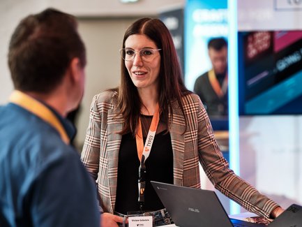 Geschäftliche Gesprächssituation zwischen einer Frau und einem Mann, im Hintergrund ein Screen