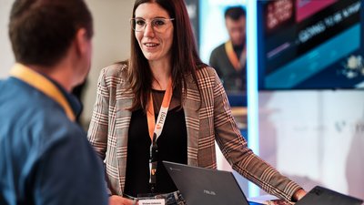 Geschäftliche Gesprächssituation zwischen einer Frau und einem Mann, im Hintergrund ein Screen